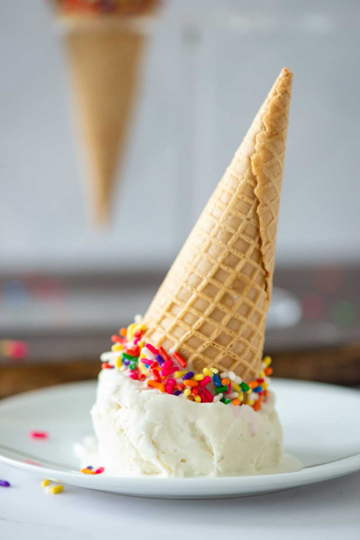 Side view of a homemade vanilla bean ice cream cone upside down and stuck onto a small dessert plate