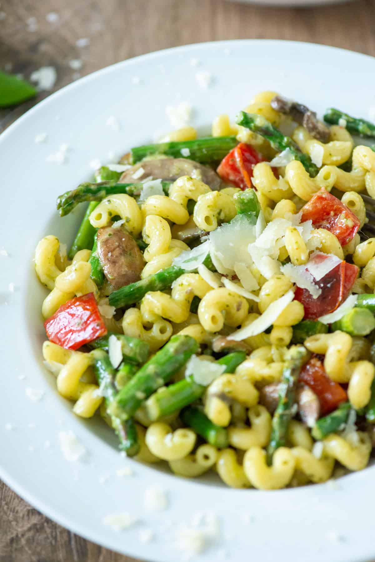 Overhead angled view of a plate of vegetable pesto pasta garnished with extra parmesan cheese