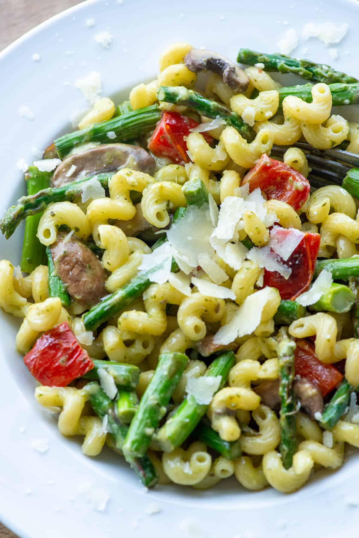 Overhead angled view of a plate of vegetable pesto pasta made with asparagus, red bell peppers and mushrooms and garnished with extra parmesan cheese