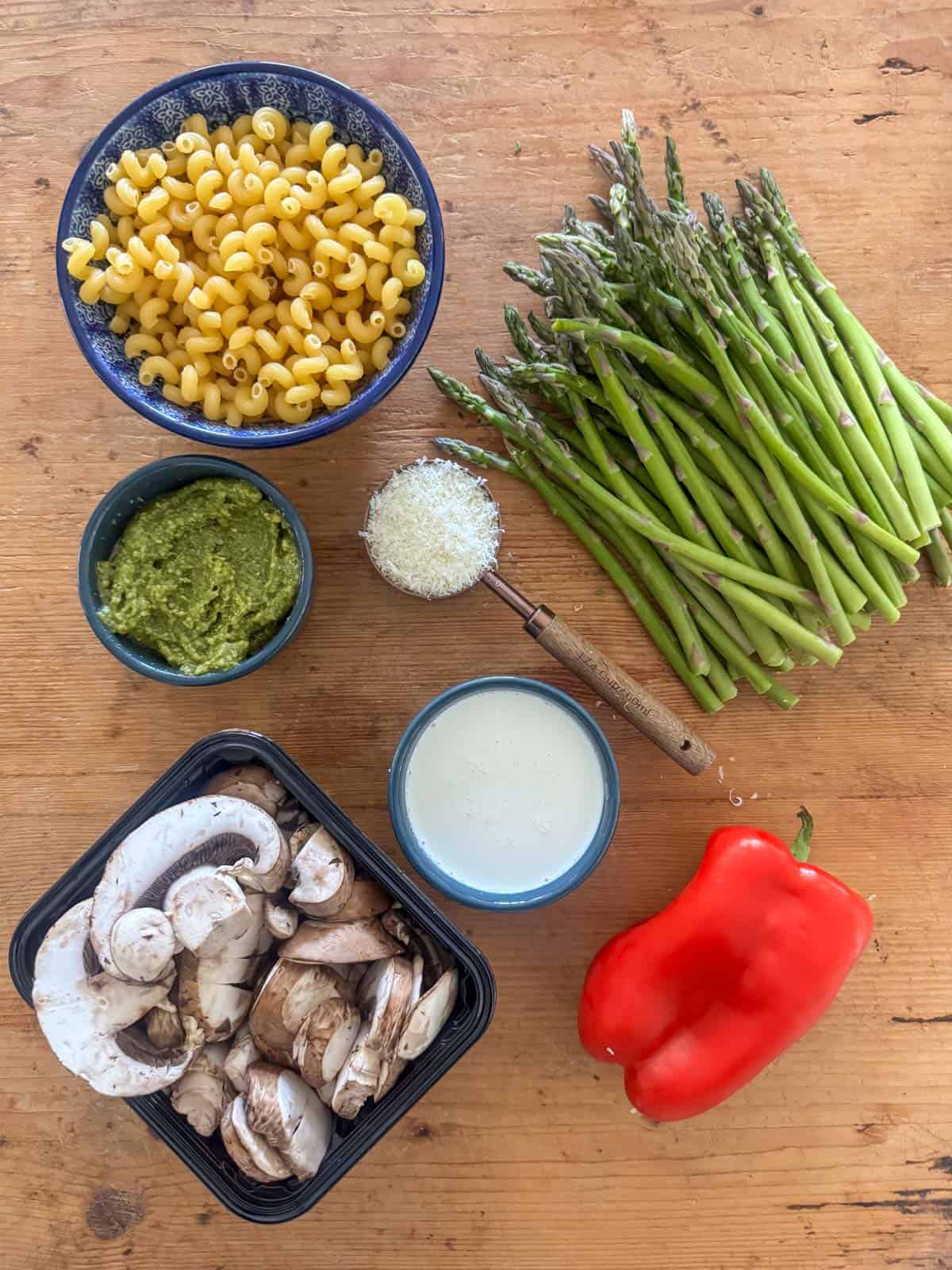 Ingredients needed to make vegetable pasta pesto: pasta, asparagus, red bell pepper, mushrooms, pesto, heavy whipping cream and parmesan cheese