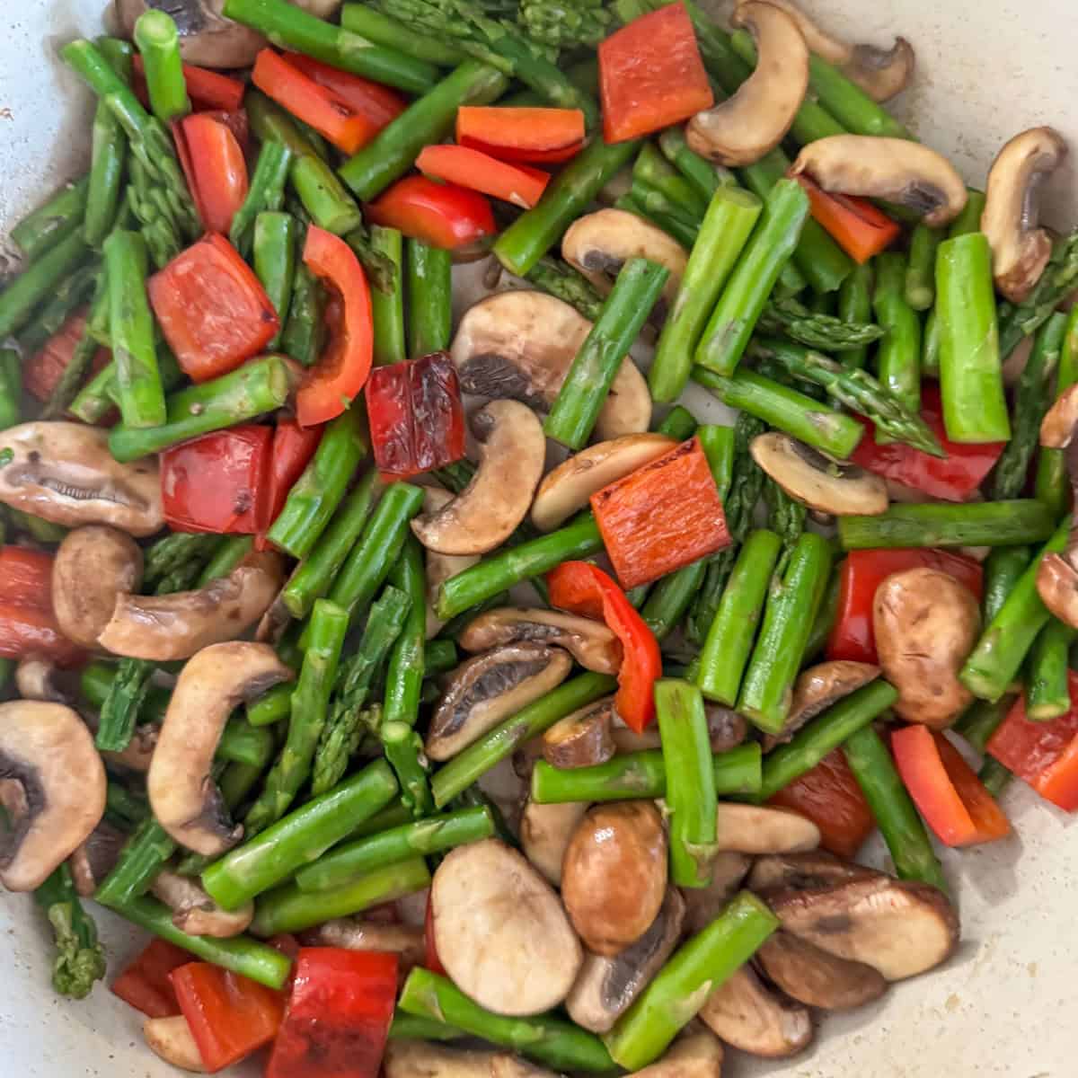 Overhead photo of stir fried red bell peppers, asparagus and mushrooms in a skillet