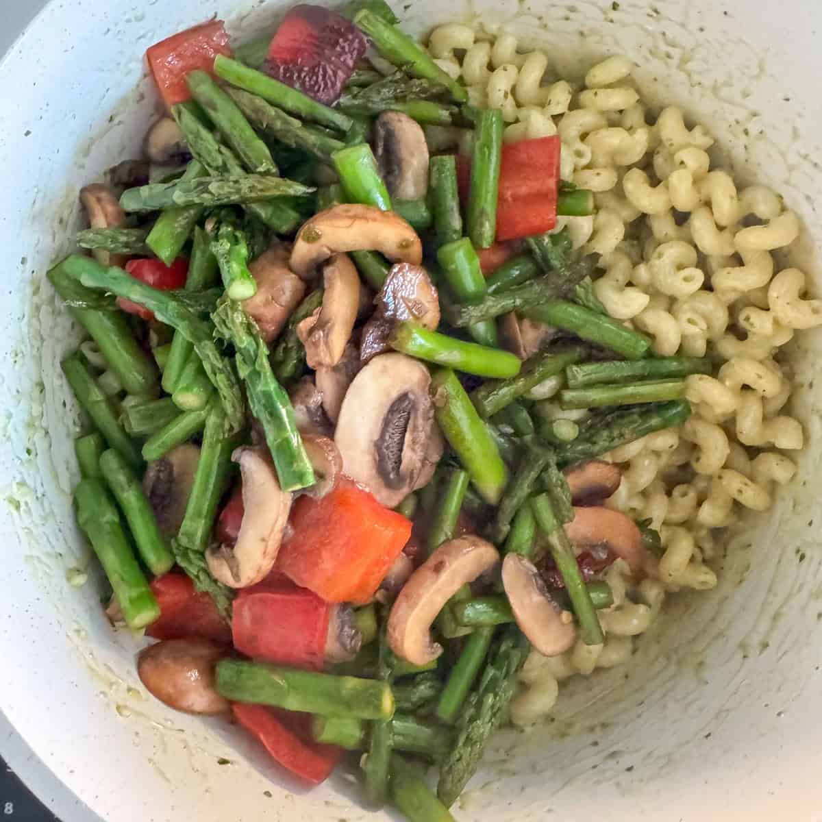 Overhead photo of cooked vegetables on top of pasta with pesto mixed in that just needs the vegetables folded in