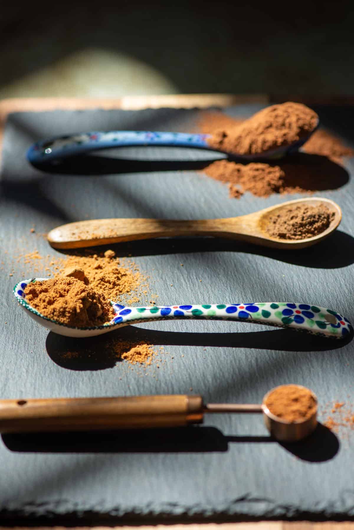 Angled side view of 4 varying types of teaspoons all with different spices on them in high contrast light