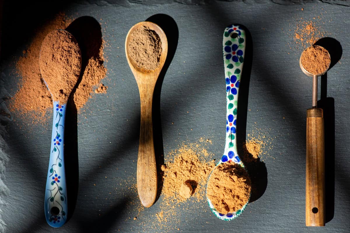 Angled overhead view of 4 varying types of teaspoons all with different spices on them in high contrast light
