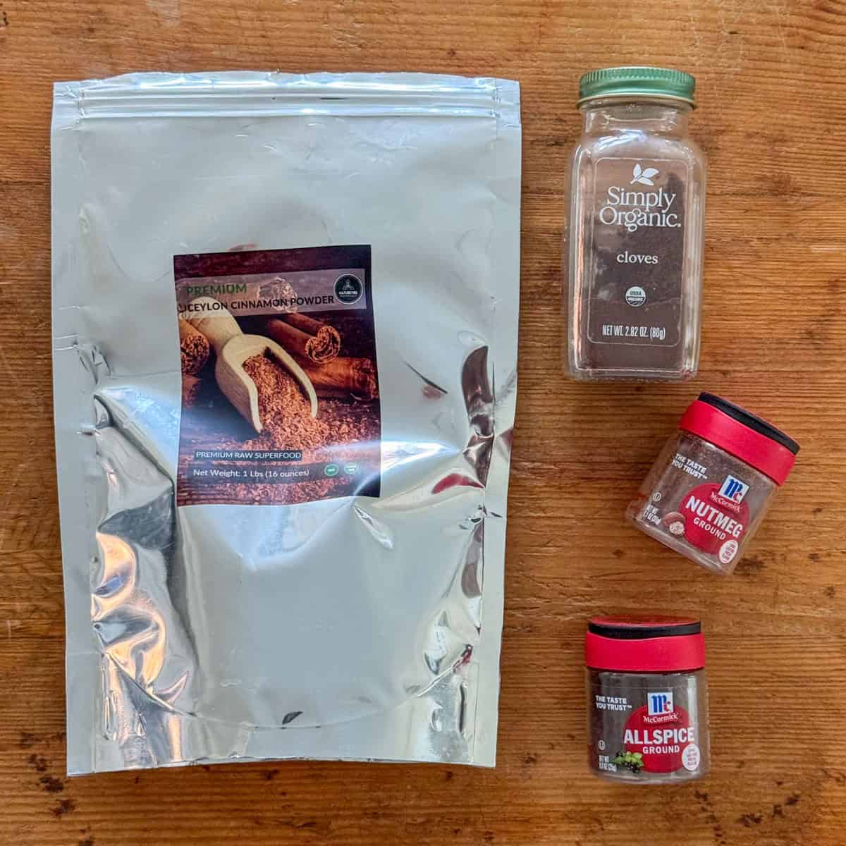 Overhead view of spices needed to make apple pie spice blend: cinnamon, nutmeg, allspice and cloves.