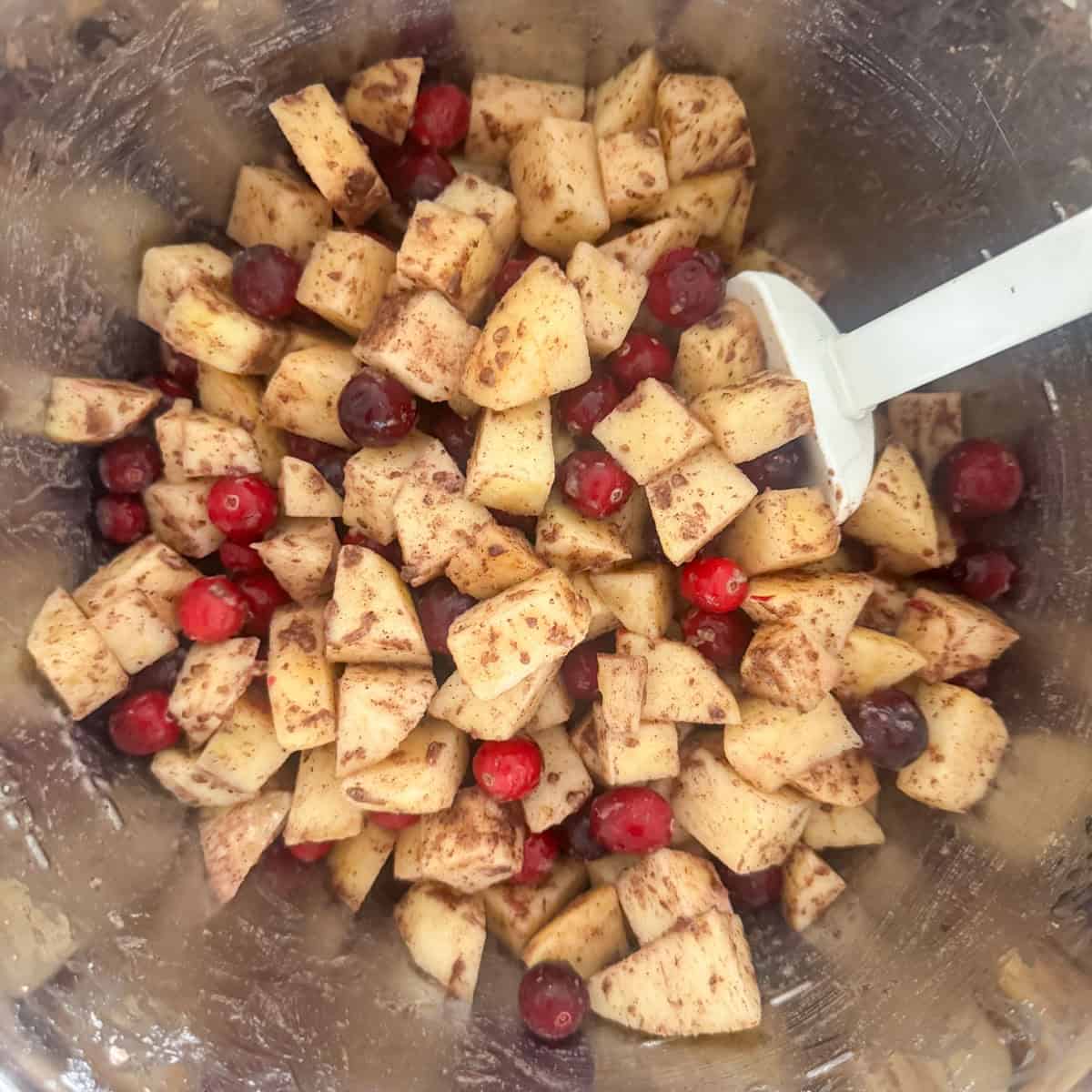 Step 1 of making a cranberry apple crumble: toss the cut apples and cranberries with the all purpose flour, brown sugar, apple pie seasoning mix and the vanilla.