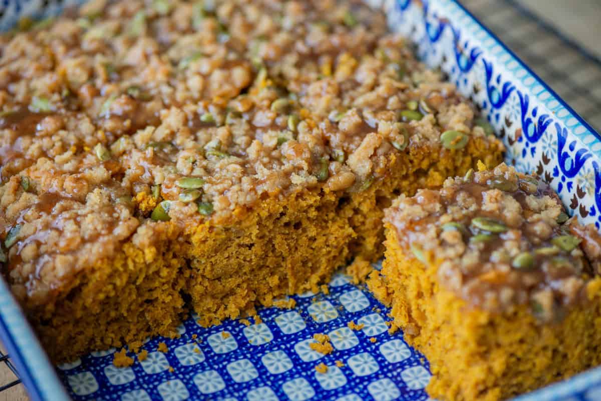 Angled overhead view of a baking pan half full of pumpkin spice coffee cake. Some pieces are missing so that you can see the texture of t