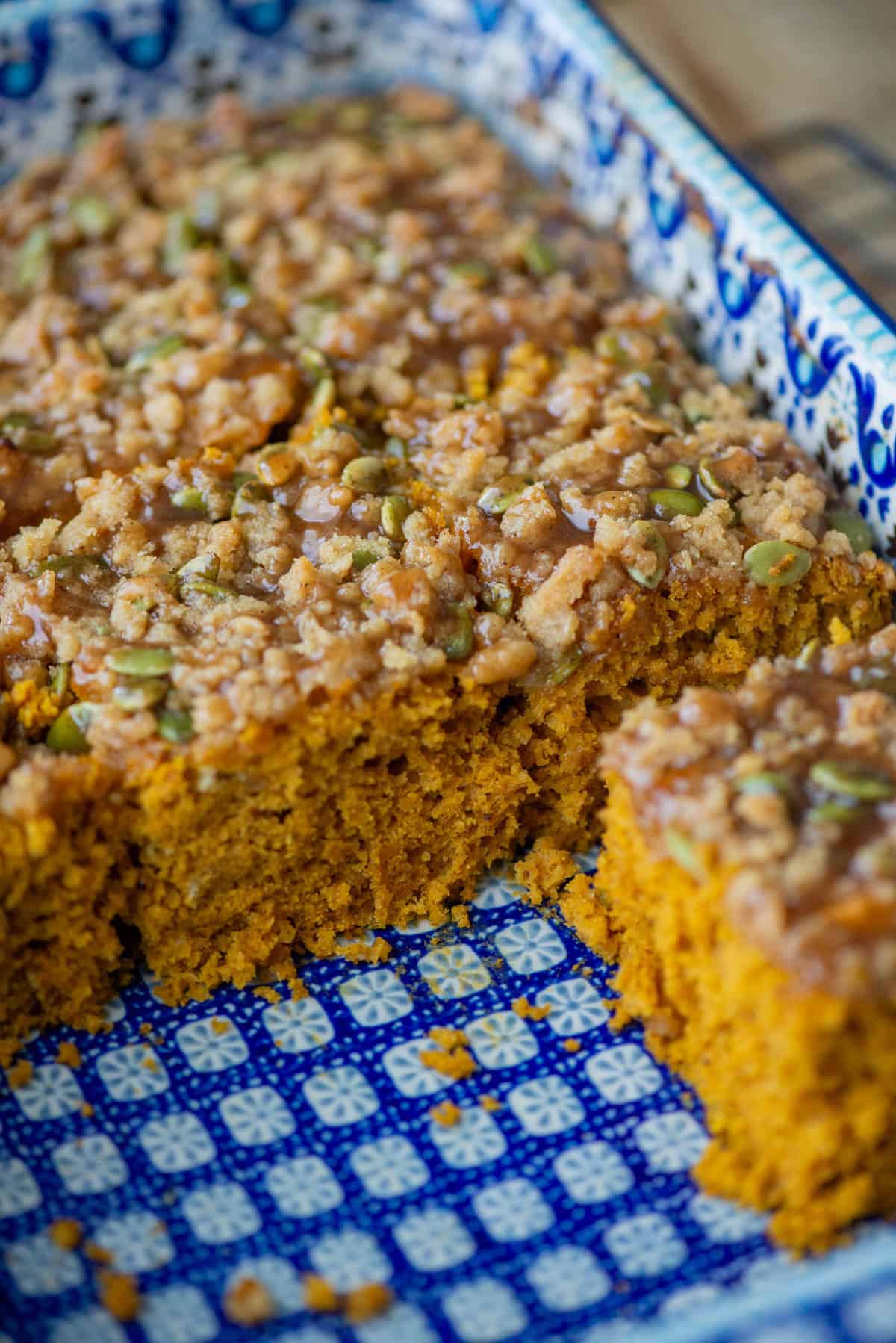 Angled overhead view of a baking pan half full of pumpkin spice coffee cake. Some pieces are missing so that you can see the texture of the cake.