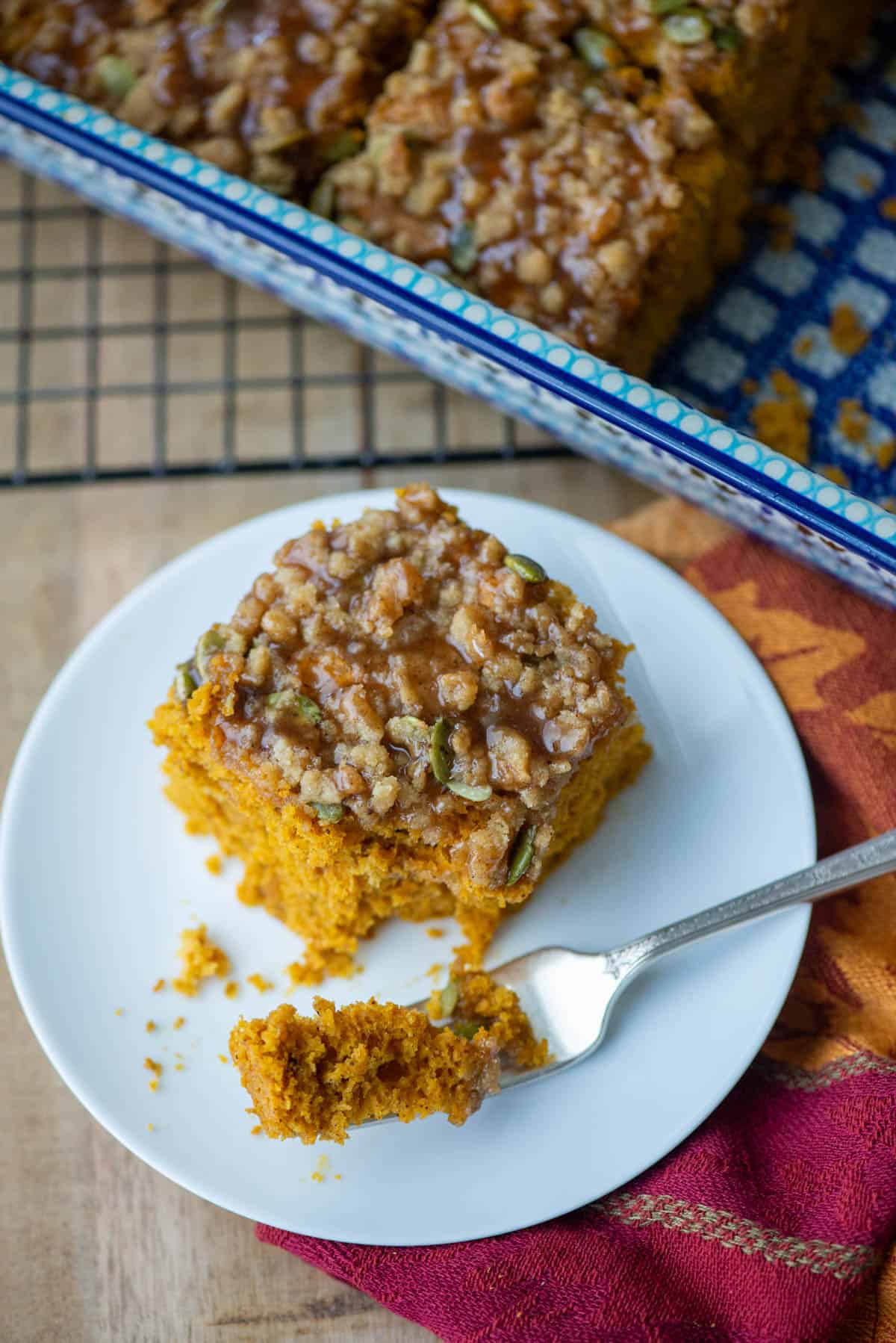 Overhead photo of a slice of pumpkin spice coffee cake on a small dessert plate with the pan of coffee cake in the background