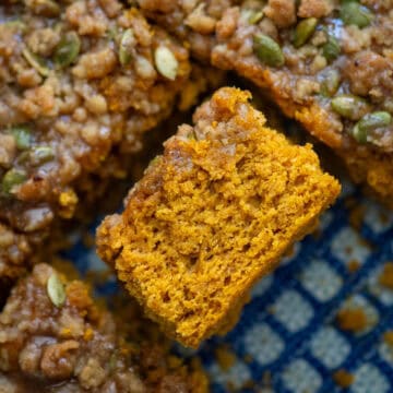 Overhead photo of easy pumpkin spice coffee cake with a pumpkin seed streusel topping and a pumpkin spice glaze that's been cut and turned on its side so that you can see the texture of the cake