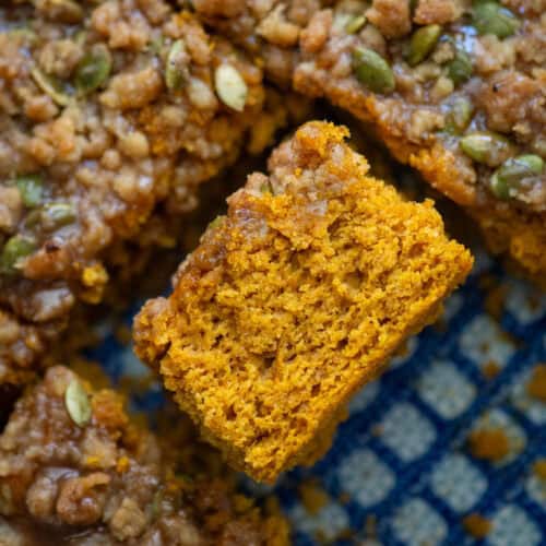 Overhead photo of easy pumpkin spice coffee cake with a pumpkin seed streusel topping and a pumpkin spice glaze that's been cut and turned on its side so that you can see the texture of the cake