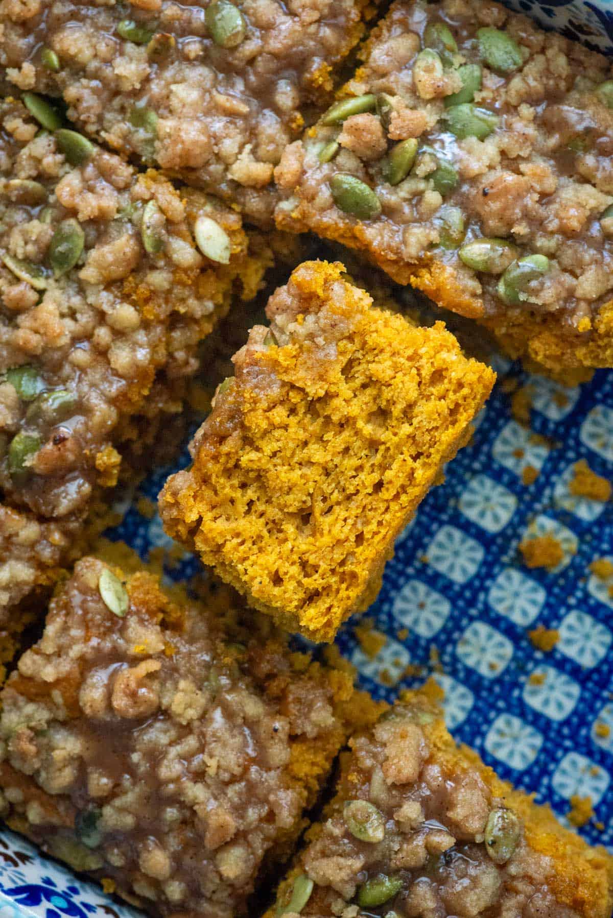 Overhead photo of easy pumpkin spice coffee cake with a pumpkin seed streusel topping and a pumpkin spice glaze that's been cut and turned on its side so that you can see the texture of the cake