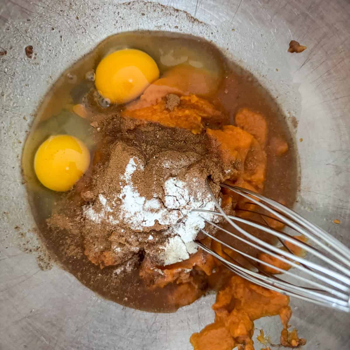 Step 1 of making pumpkin coffee cake: add pumpkin puree, water, eggs, pumpkin pie spice and baking soda to a large mixing bowl