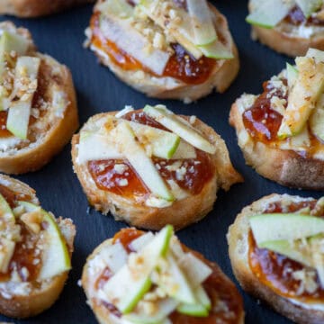 Close up overhead photo of apple, goat cheese and fig jam crostini on a slate platter