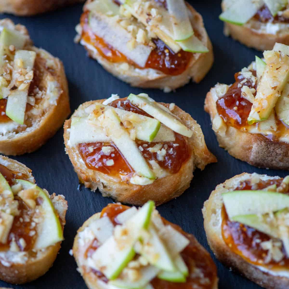 Close up overhead photo of apple, goat cheese and fig jam crostini on a slate platter