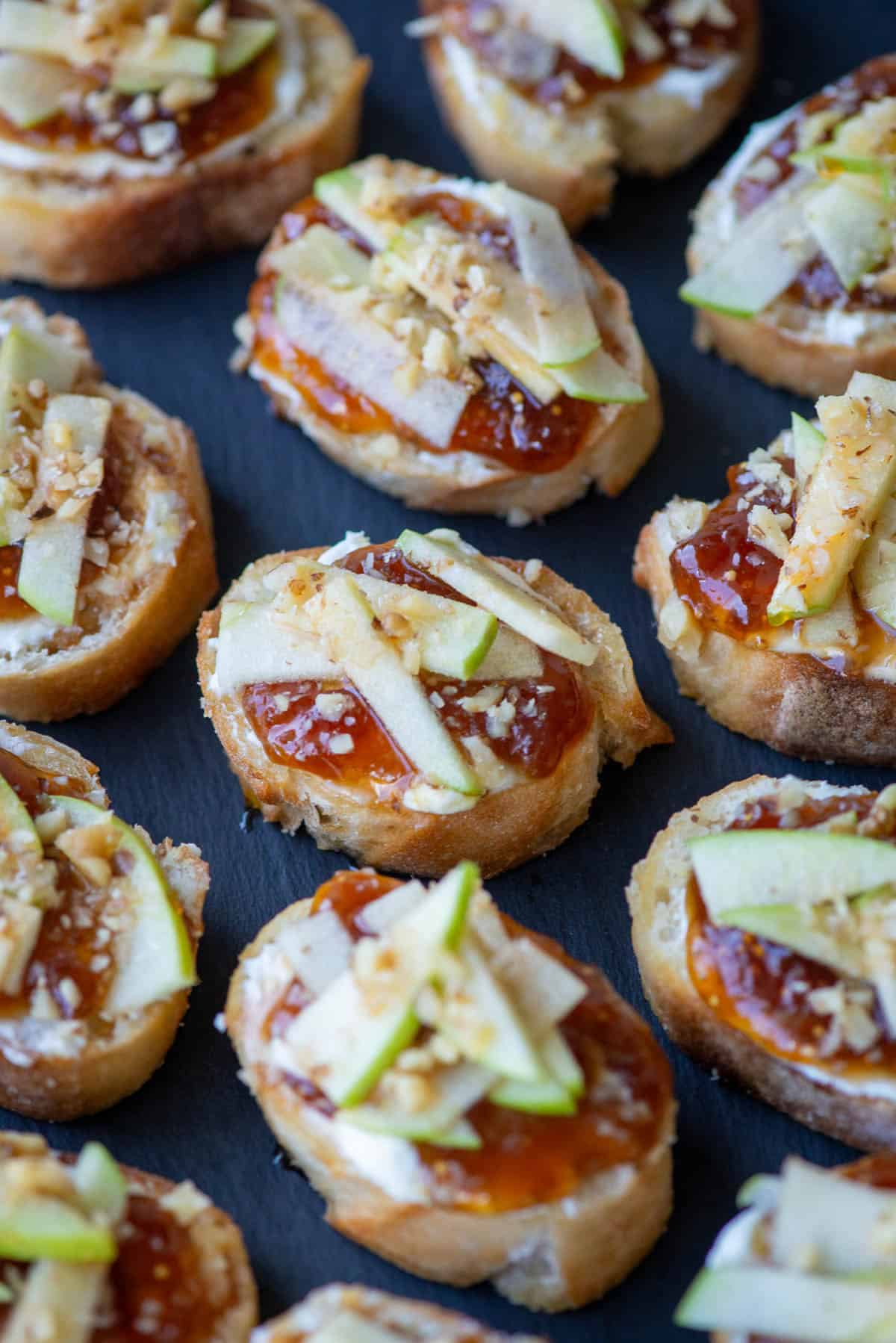 Close up overhead photo of apple, goat cheese and fig jam crostini on a slate platter