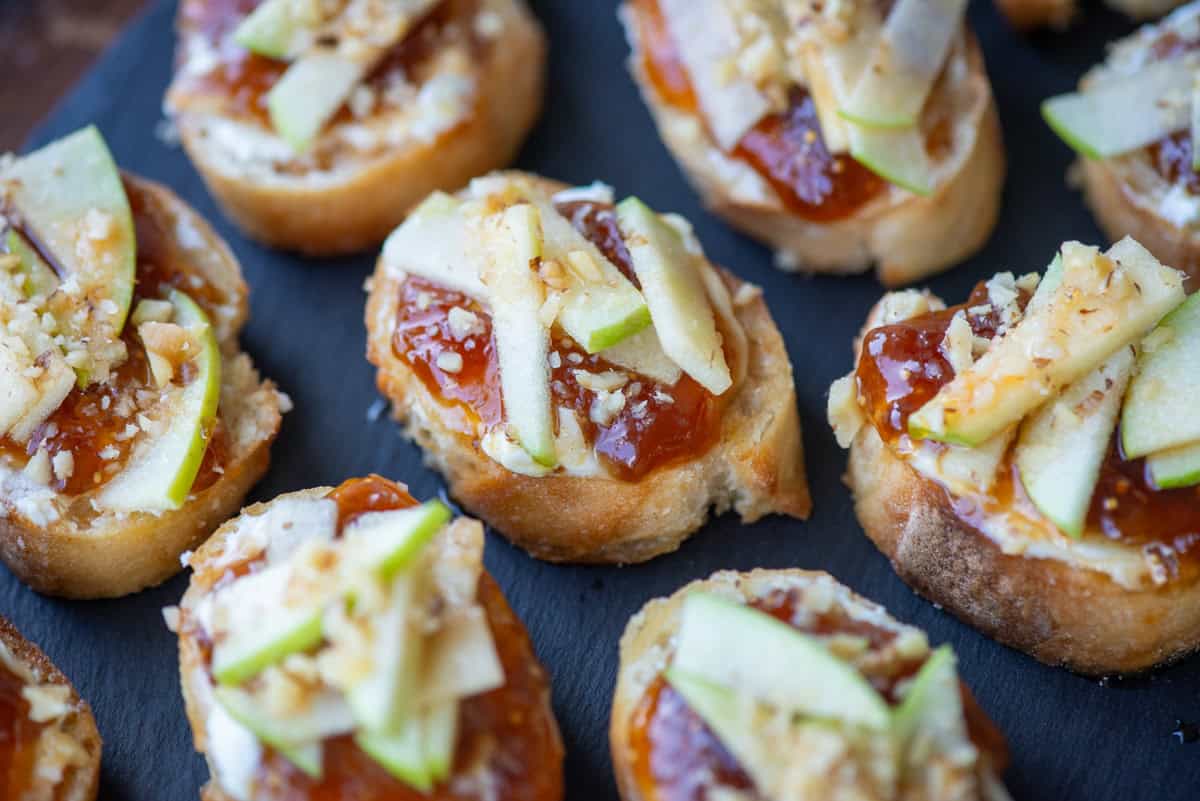 Close up overhead photo of apple, goat cheese and fig jam crostini on a slate platter
