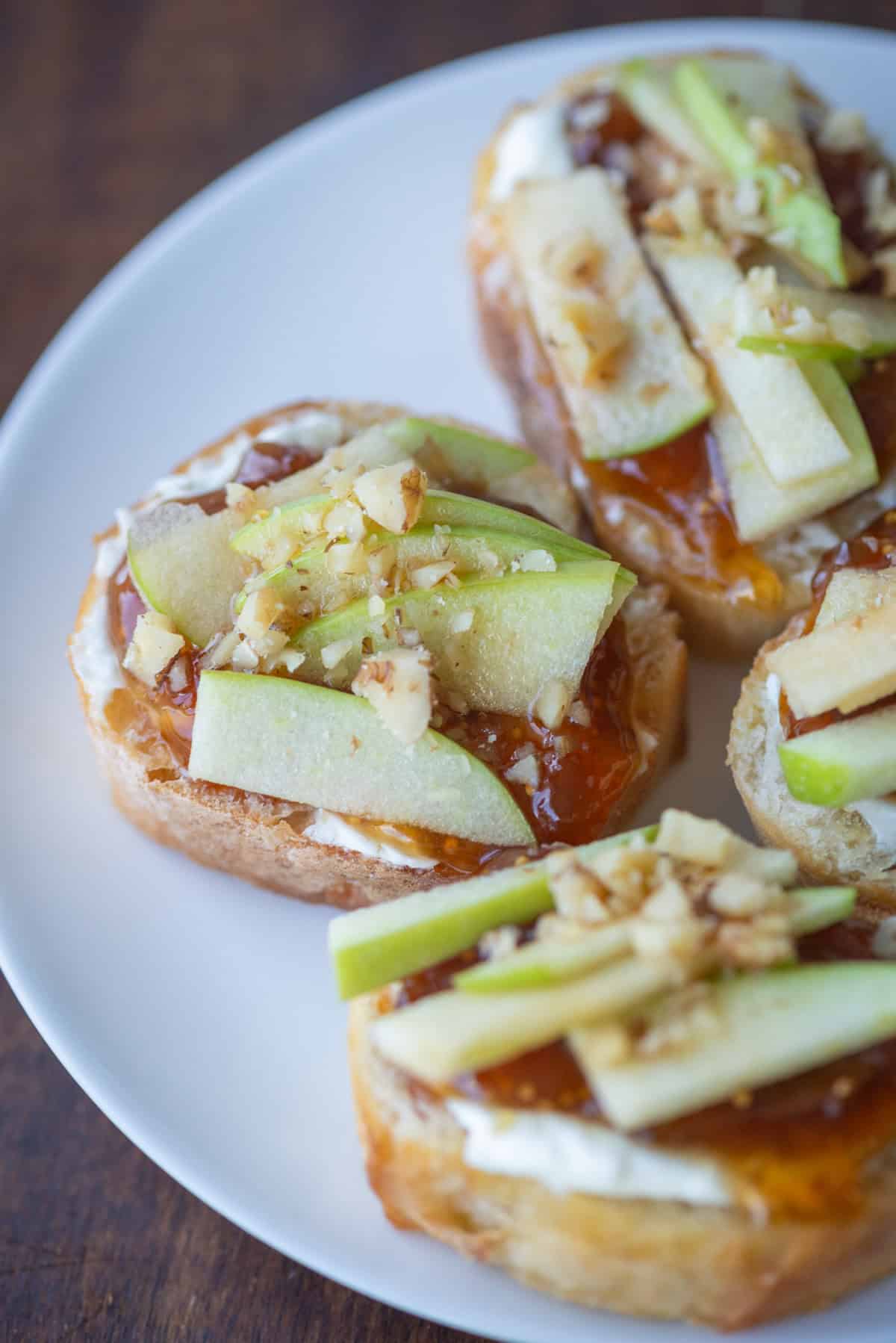 Close up overhead angle photo of apple, goat cheese and fig jam crostini on a white appetizer plate