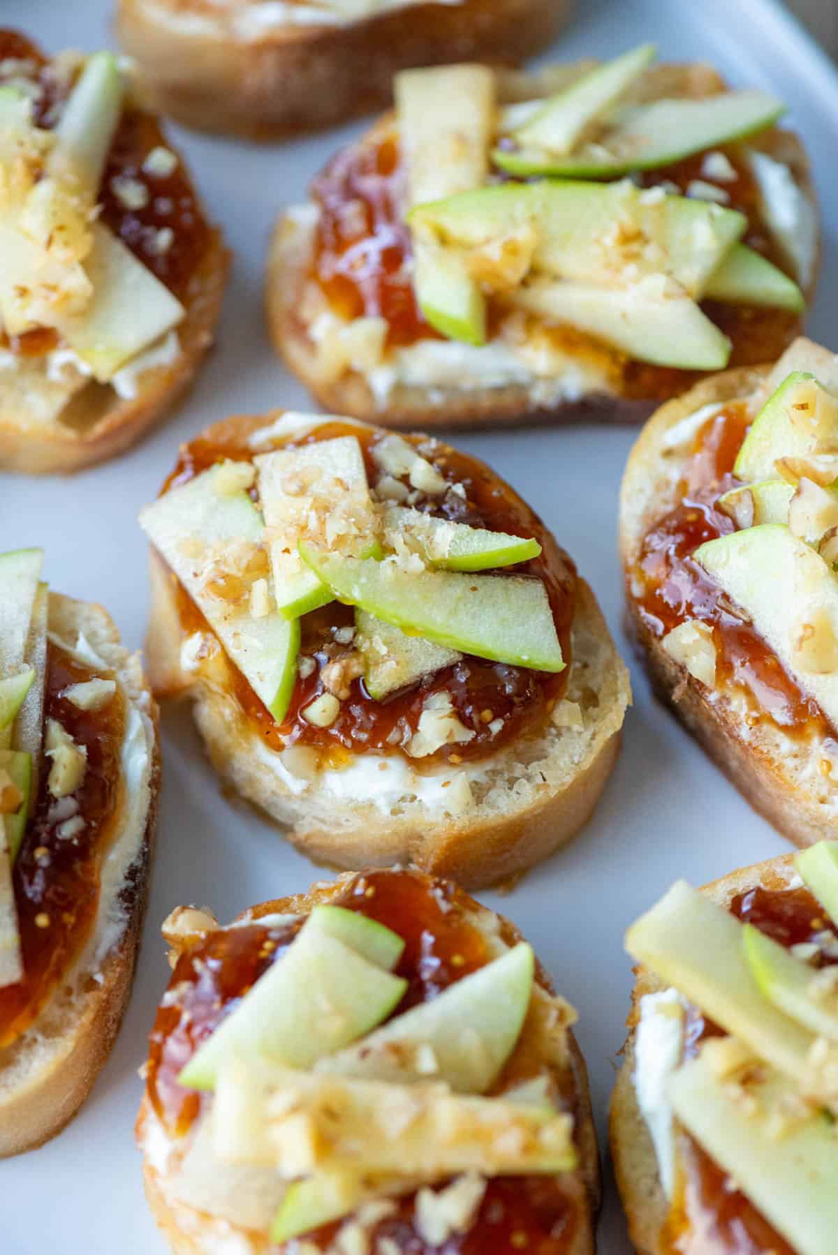 Close up overhead view of apple, goat cheese and fig jam crostini on a white platter