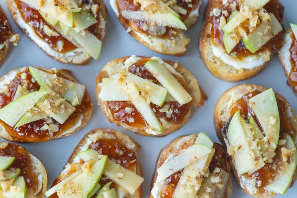 Close up overhead view of apple, goat cheese and fig jam crostini on a white platter