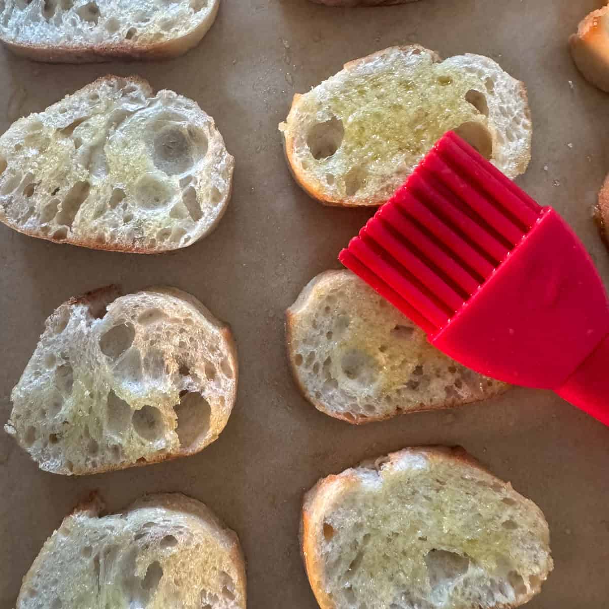 Overhead photo of brushing cut baguette slices with olive oil
