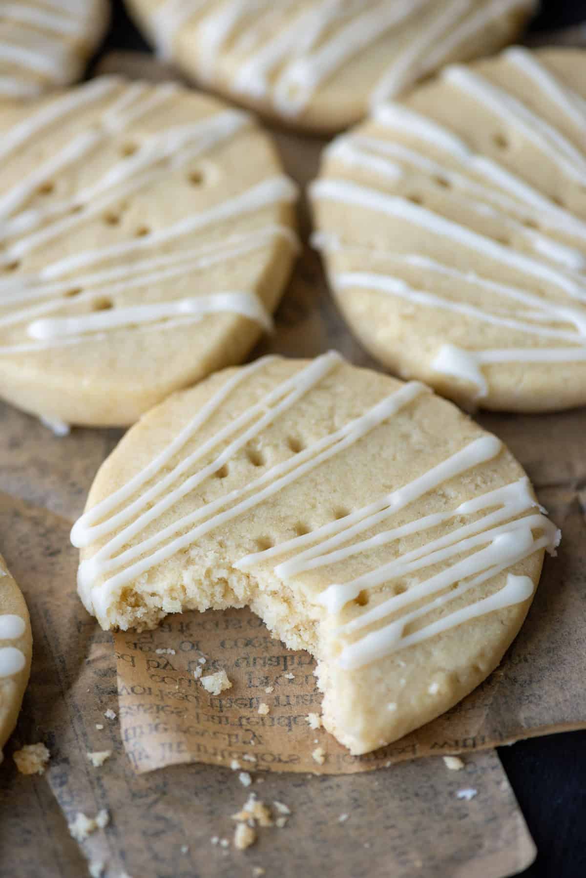 Overhead view of dairy free shortbread cookies on a plate covered with newspaper parchment paper where the front cookie has a bite taken out