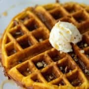 Overhead angled view of a part of a pumpkin spice waffle topped with whipped butter, maple syrup and chopped pecans with a title overlay that says Pumpkin Spice Waffles at the top and another that says www.nextlevelbaker.com at the bottom.
