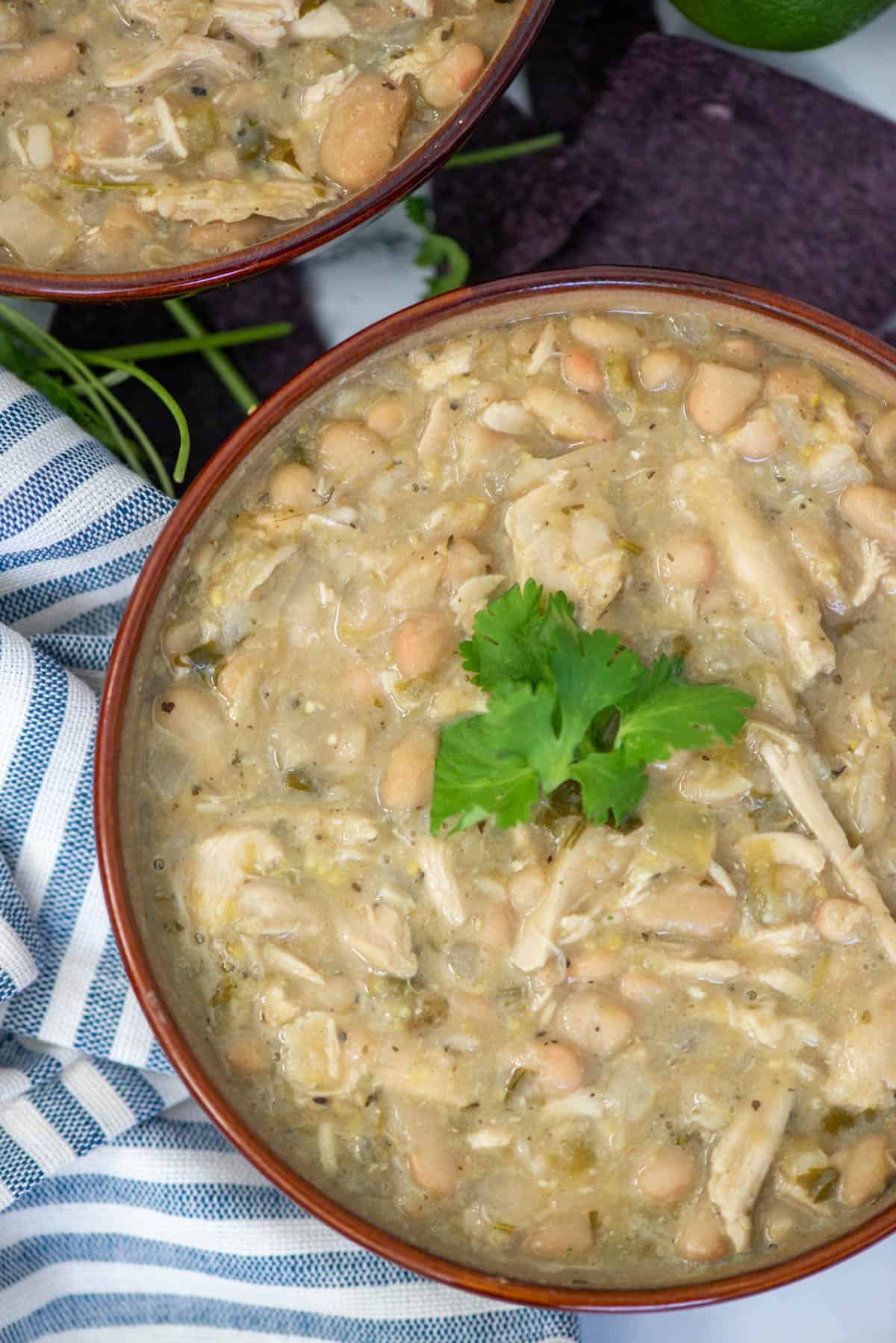 Overhead view of a partial bowl of turkey and white bean chili garnished with cilantro with another bowl visible in the background