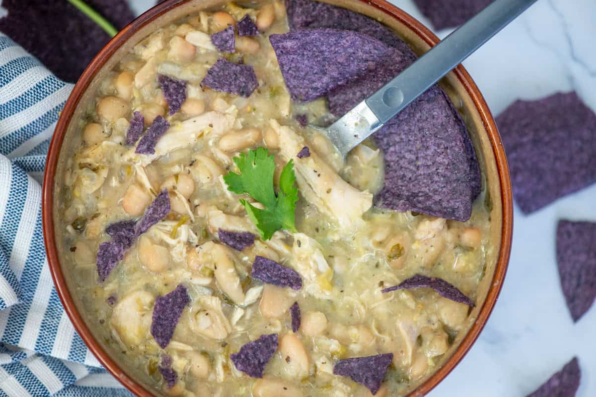 Overhead view of a bowl of turkey and white bean chili garnished with cilantro and crumpled blue corn tortilla chips